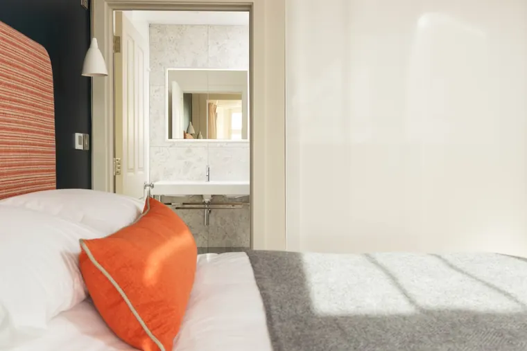 A bedroom at No.9 with a striped headboard against deep blue panelling, looking through an open door to the en-suite beyond
