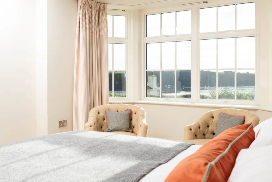 A bedroom at No.9 with a bay window over the moorings, two tub chairs and the end of the bed