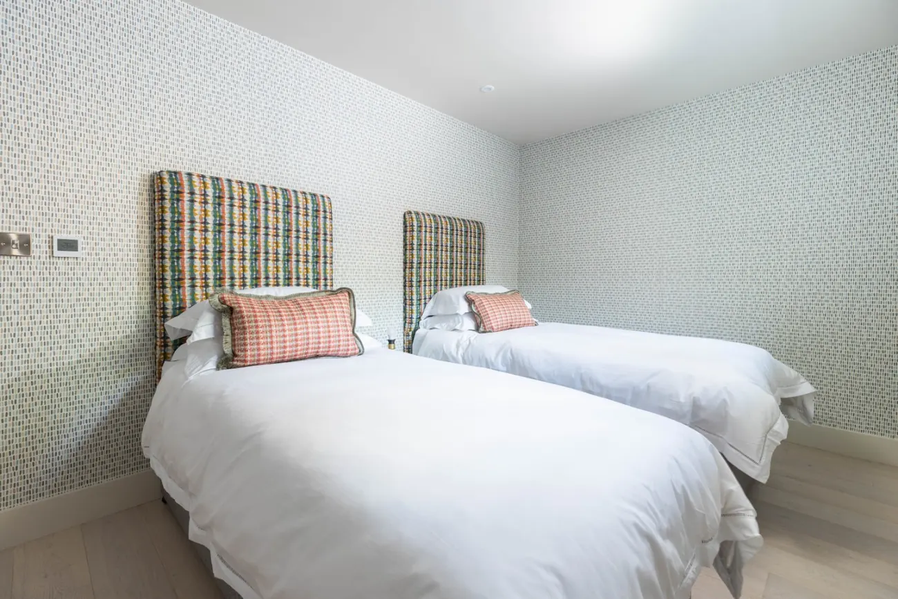Twin room with two single beds, tall woven headboards and a small-patterned wallpaper