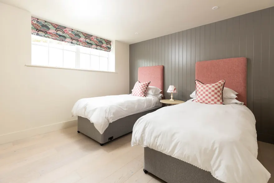 A second twin room with pink upholstered headboards against grey panelling