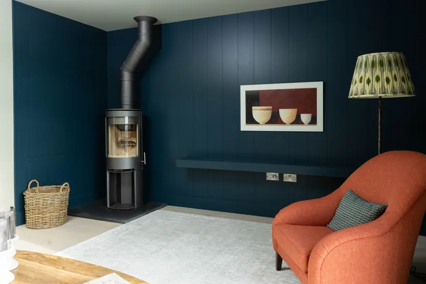 A wood burner against deep blue panelling at the far end of the sitting room, with a wicker log basket beside it