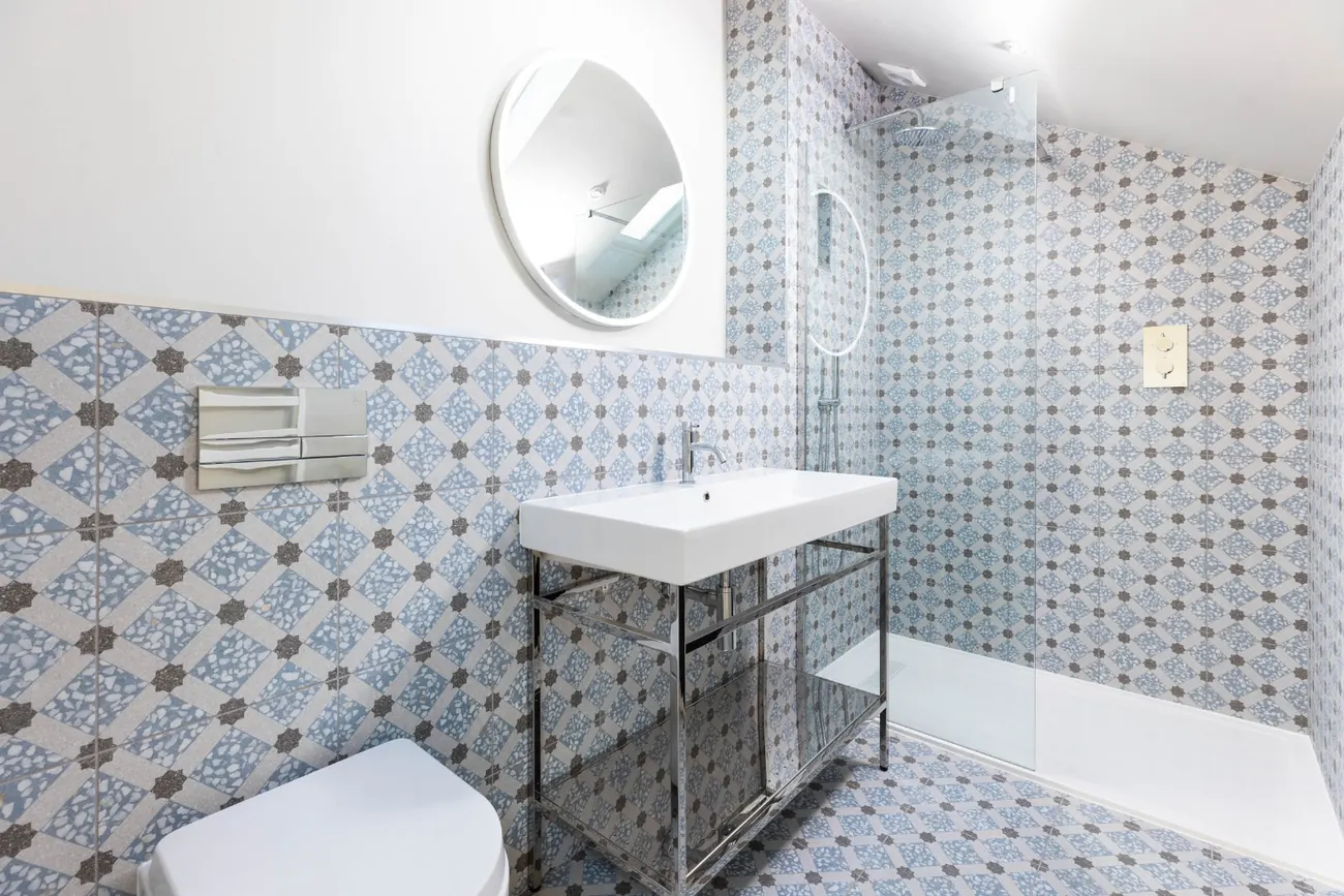 Principal en-suite with blue patterned tiles, a walk-in shower and a washstand below a round mirror